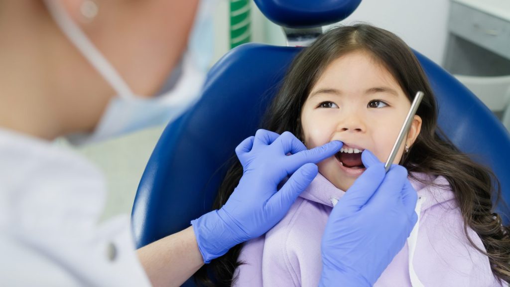 Niña en la silla del dentista para una revisión de caries en los dientes de leche.